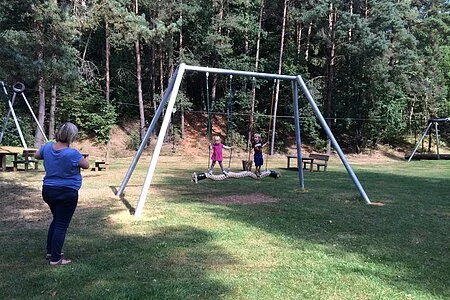 Mutter schaut den beiden Kindern beim schaukeln zu.