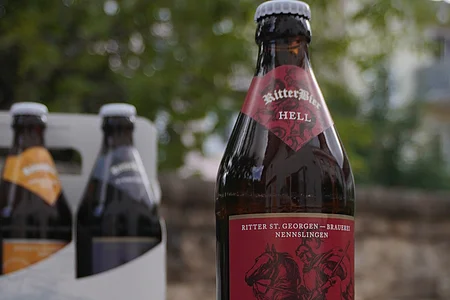 Eine Flasche Ritter Bier Hell steht auf einer Steinmauer, im Hintergrund ein Six Pack mit weiteren Flaschen.