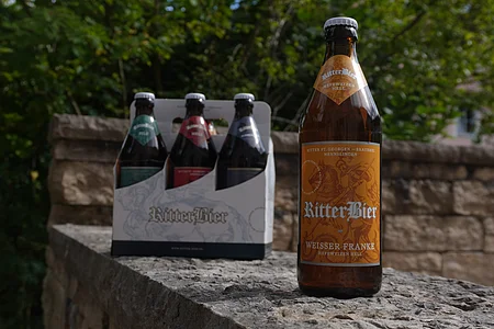 Eine Flasche Ritterbier und ein Sechserpack stehen auf einer Steinmauer im Freien.